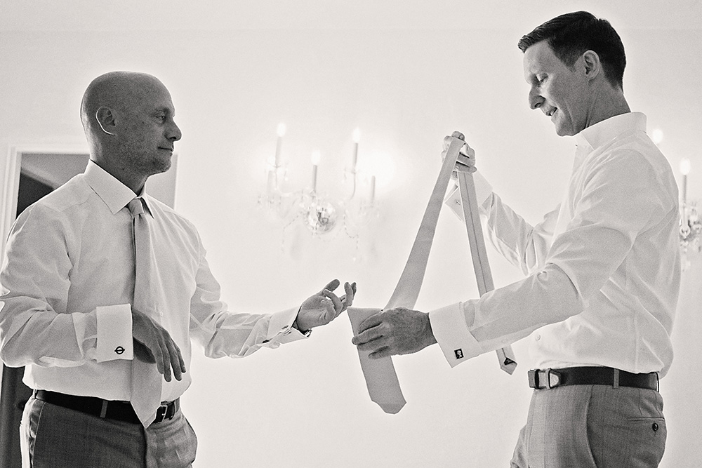 Two grooms getting ready together in a black and white photo, one helping the other with his tie before their intimate wedding at the Avalon Hotel in Palm Springs.
