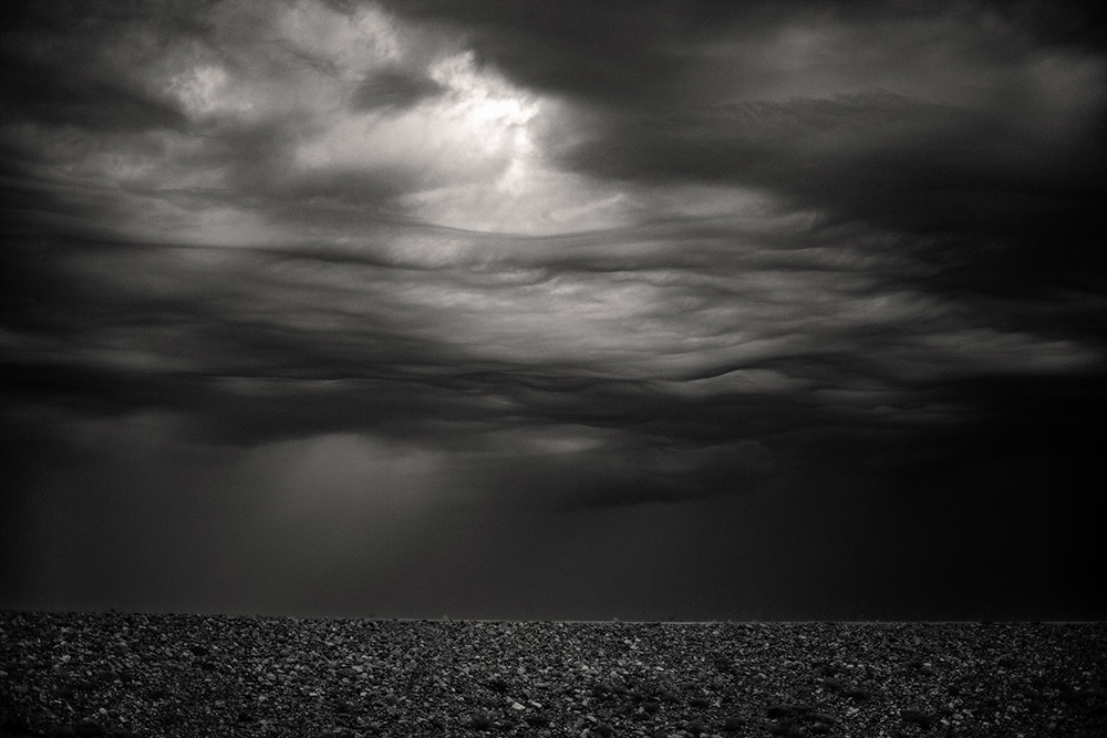 Black and white photograph of torm clouds and a rocky dam
