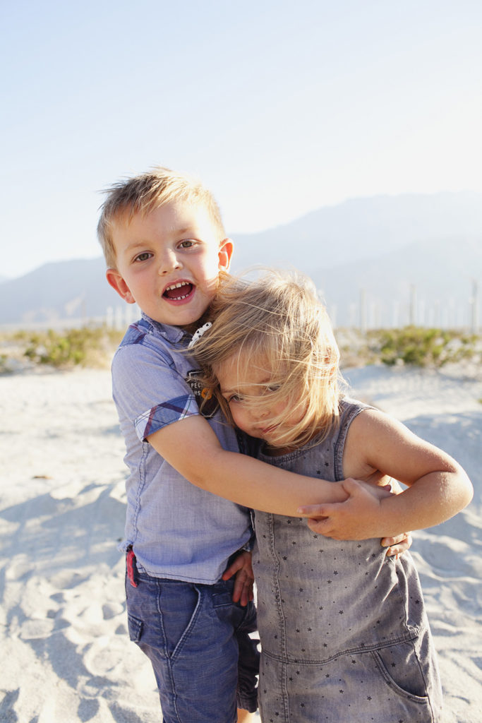 Two toddlers smile and hug in the desert
