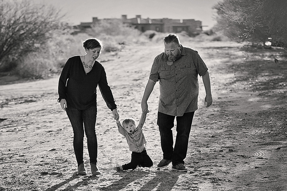 Mother and father holding hands with their toddler as he trips in the desert