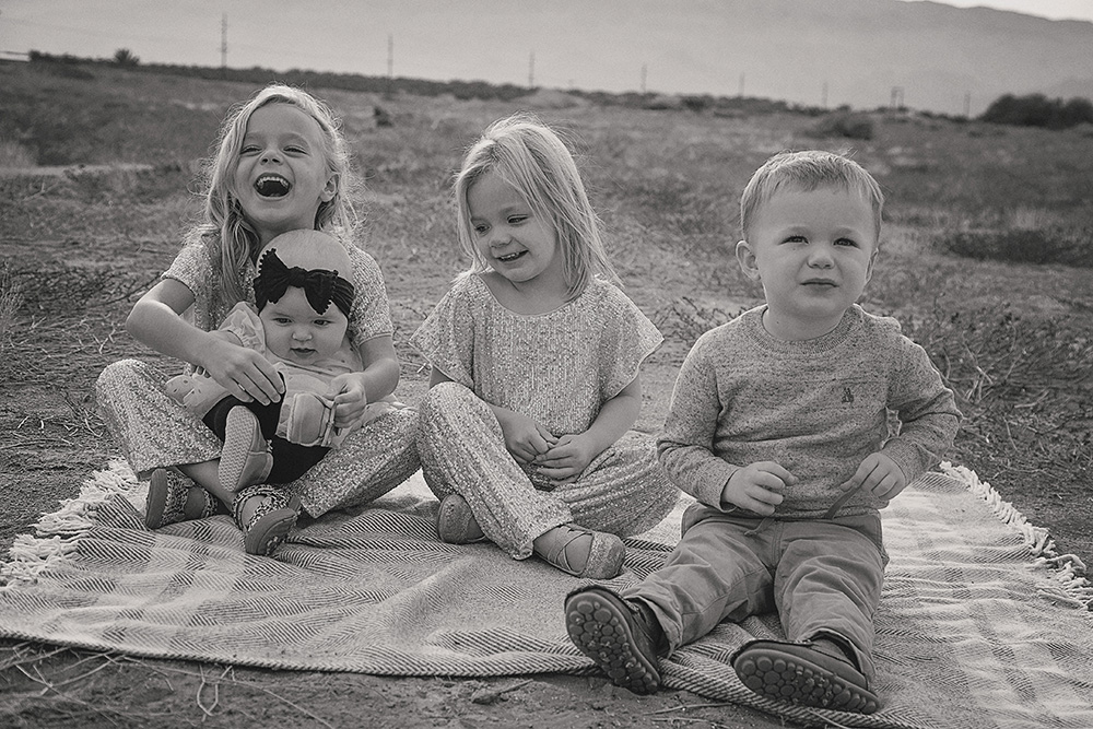 Black and white photograph of 4 childred seated on a blanket in the desert