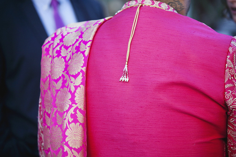 Details of the back of the grooms coat, including a gold chain and pink and gold sari
