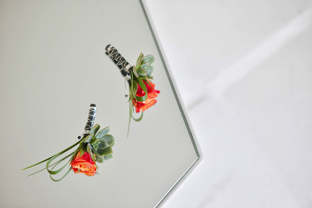 Two boutonnieres made with orange roses and a single succulent lay on a glass table